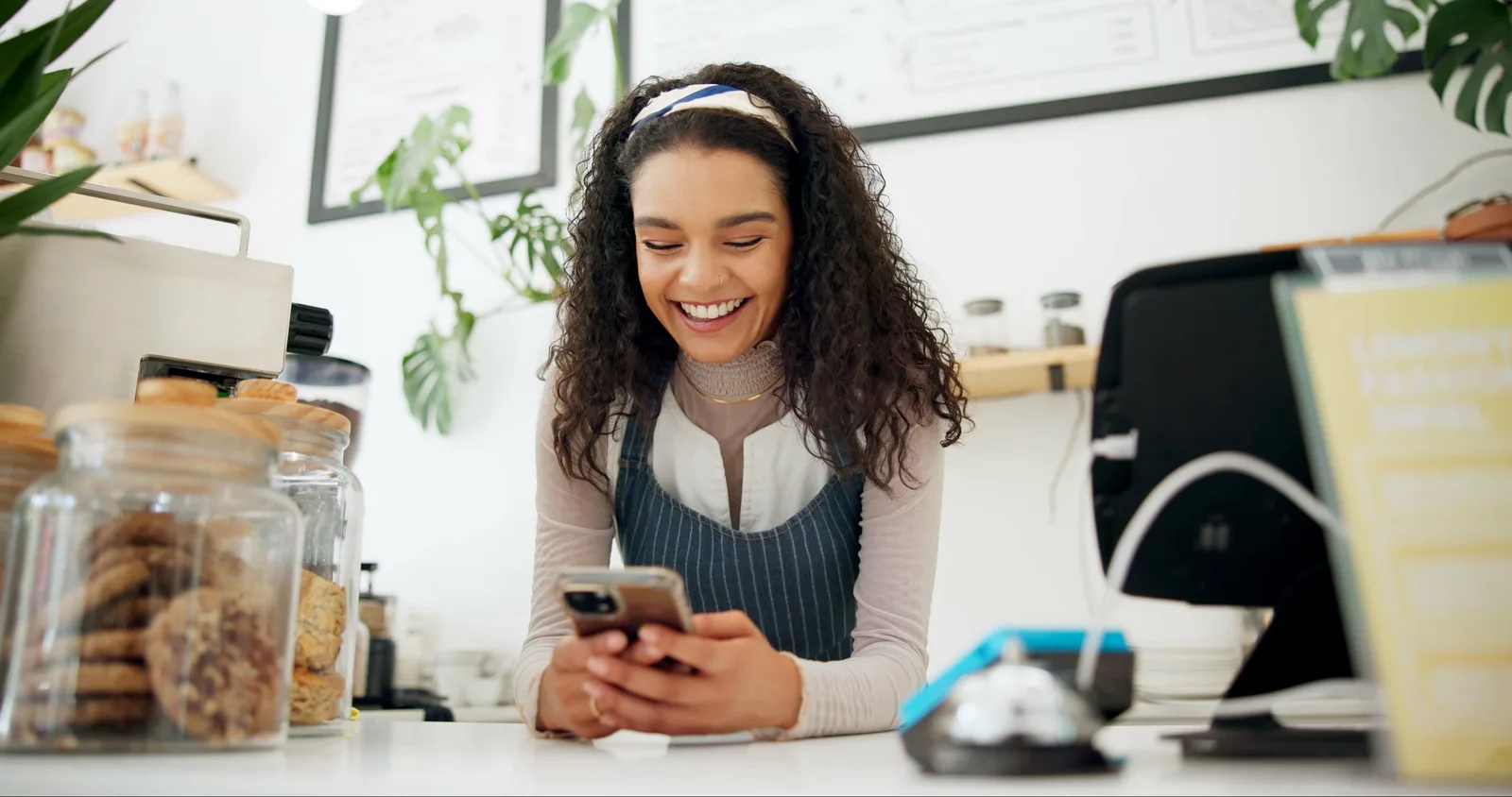A barista behind the counter smiles at a customer message on her phone