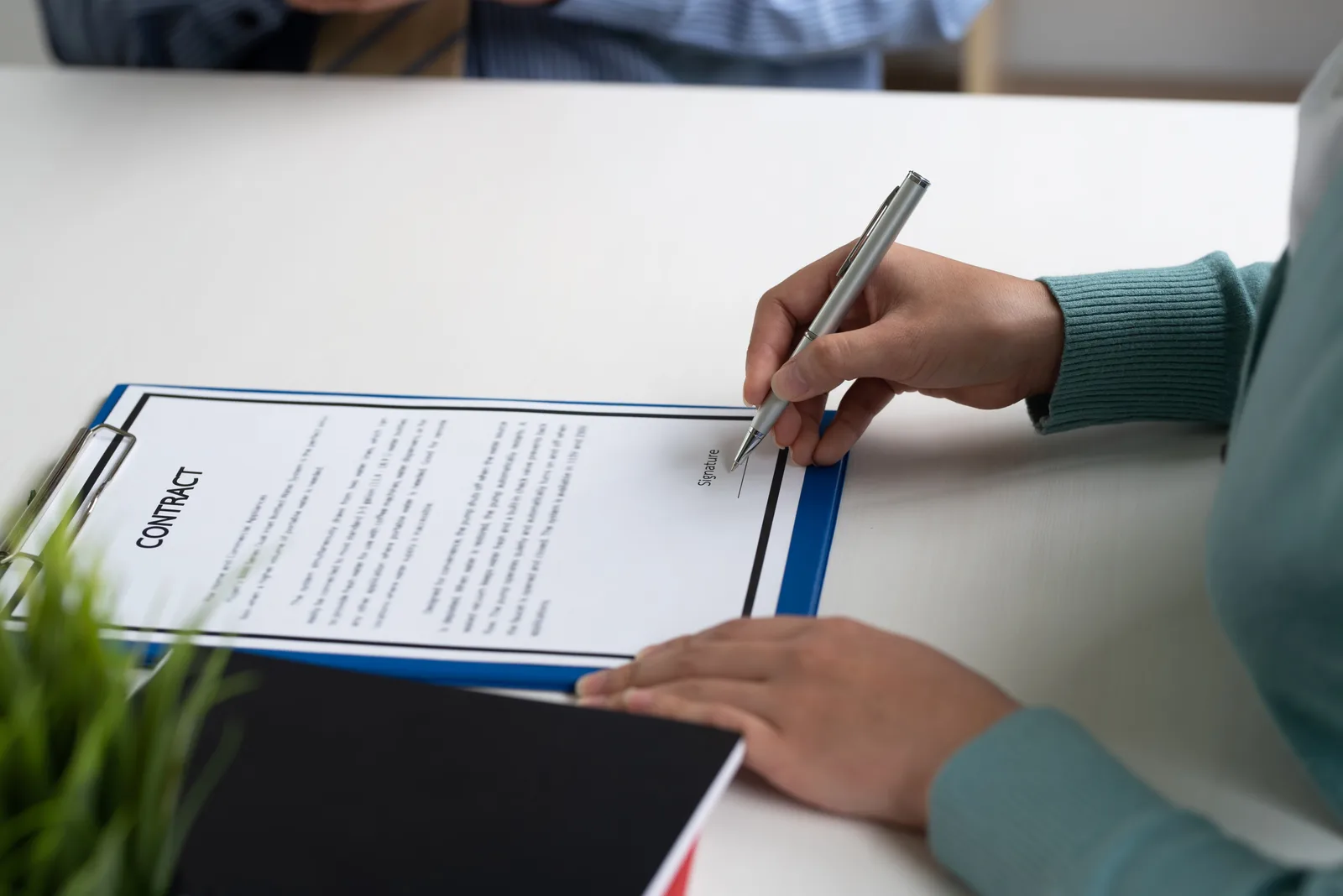 A woman's hand with a pen about to sign a contract on a clipboard, the consent that keeps outreach legal