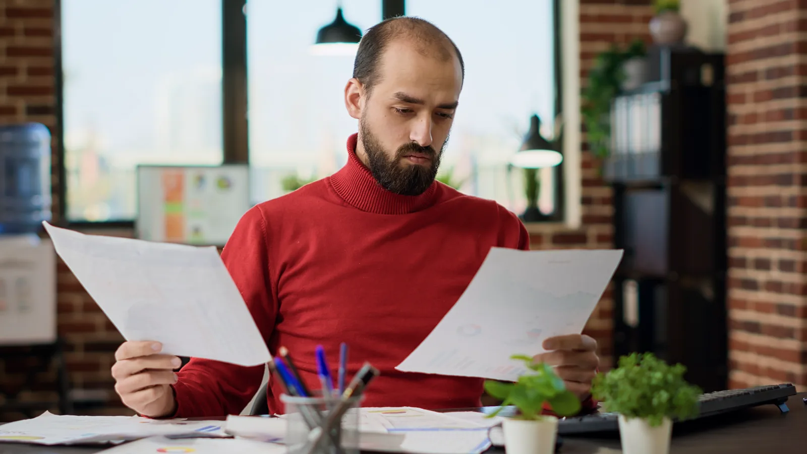 Owner at a desk comparing two printed proposals side by side, with a calculator beside them