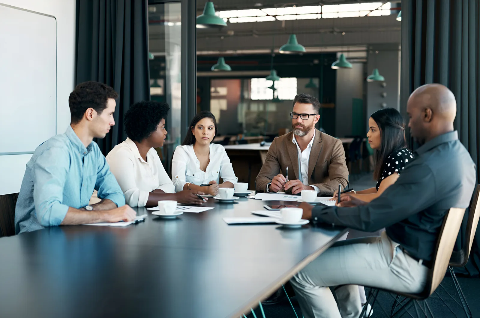 Six colleagues around a long meeting table with coffee cups and notes during a planning session