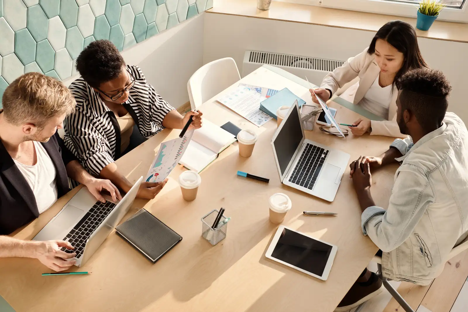 Three managers in a bright office debate a plan over laptops and printed pages