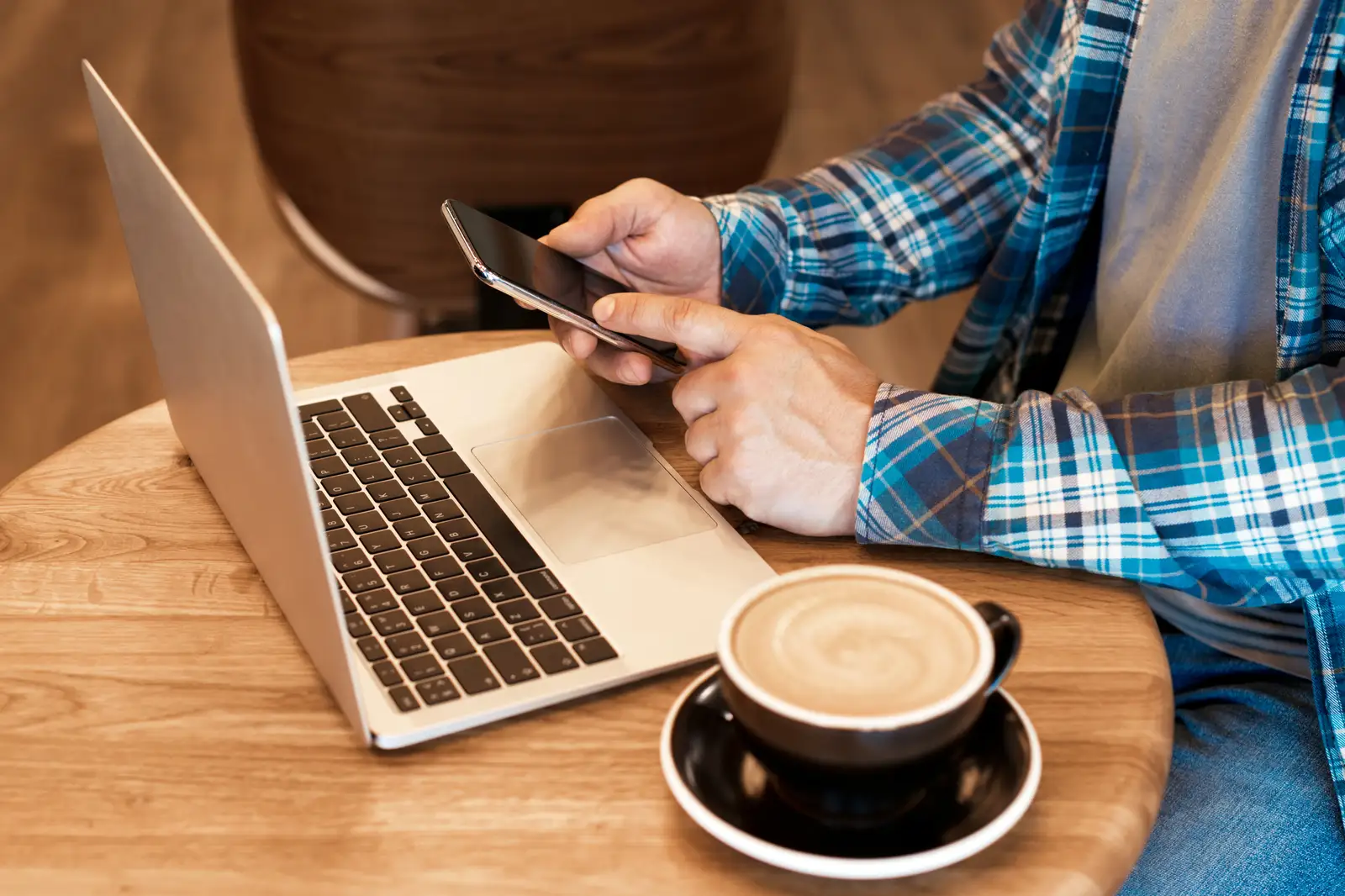 A freelancer at a cafe table with his laptop, phone and coffee, running the morning's operations