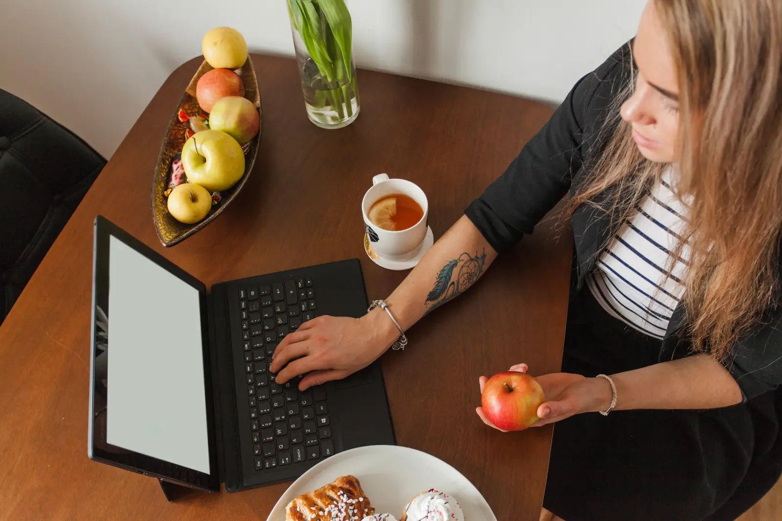 Woman typing a draft on a laptop with a kitchen timer and a coffee mug beside her
