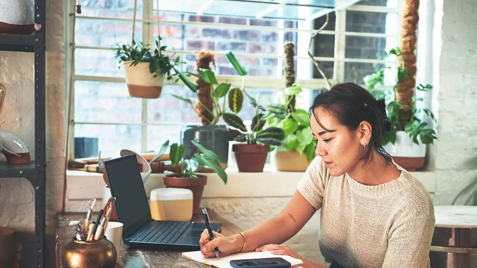 Small business owner writing on a large wall calendar next to an open laptop on a wooden desk