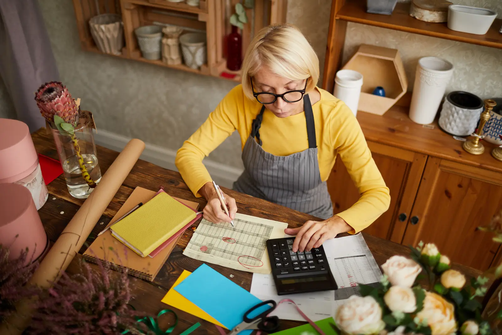 Owner working out a monthly budget with a calculator and a printed spreadsheet at a table