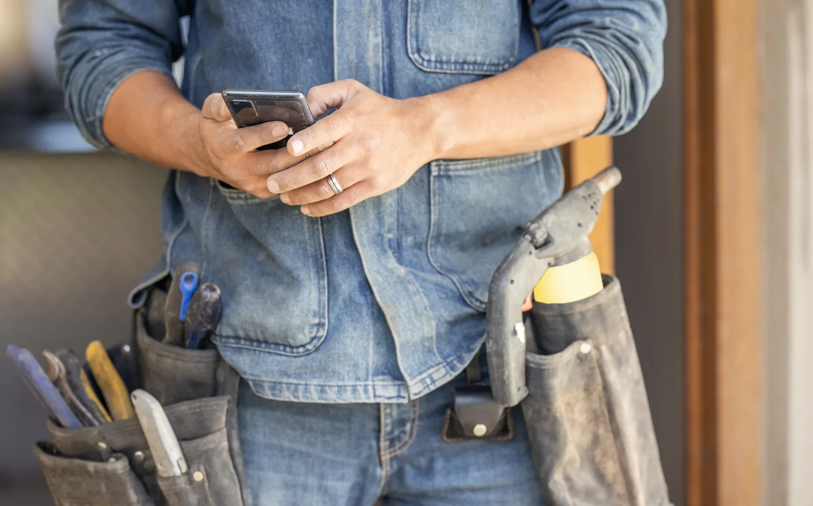 A plumber with a tool belt checks his phone between jobs