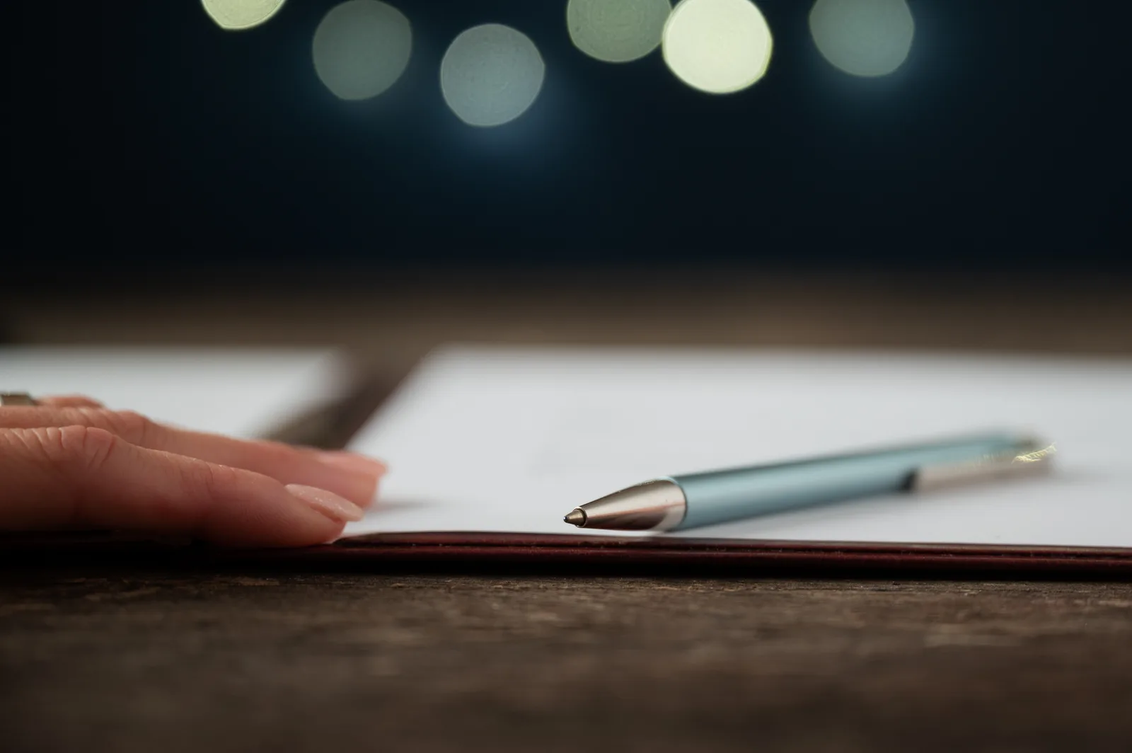 A hand rests on a contract page beside a pen, reading the fine print line by line