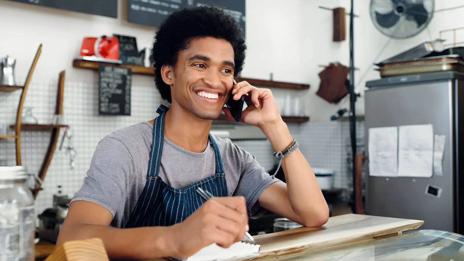 A cafe owner smiles at a call on her phone behind the counter, the reply a GoHighLevel automation sent before she could