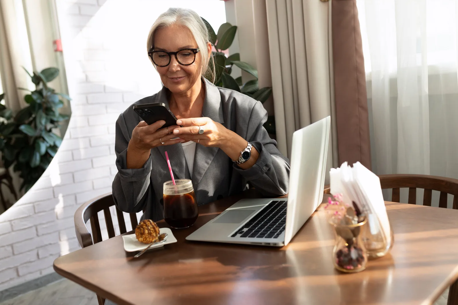 A business owner at a cafe table works through her old customer list on a laptop, phone in hand