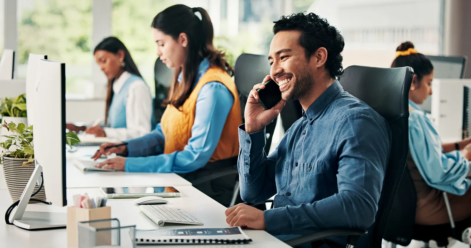 A salesman takes a routed call at his desk while colleagues work behind him