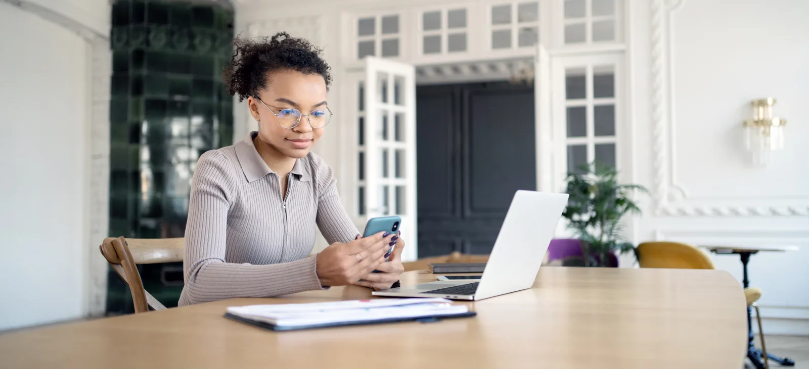 A real estate agent replies to a client by text at her desk, laptop and listing sheets in front of her