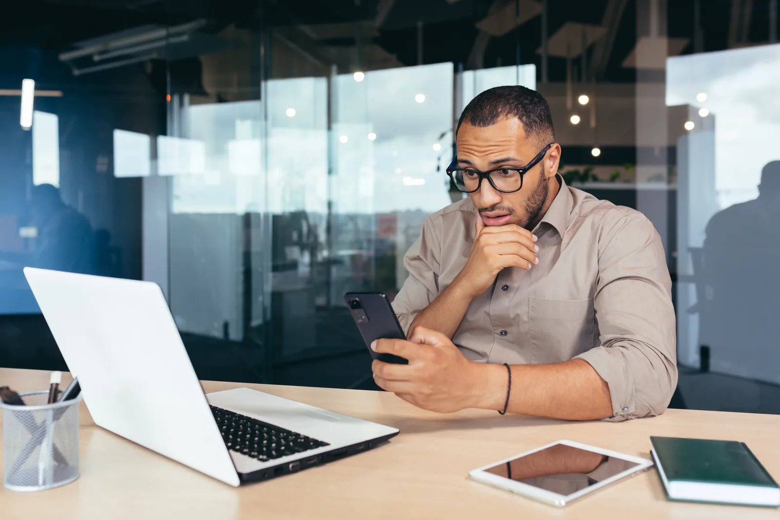 A business owner at his laptop reads a message on his phone, working out why a text never sent