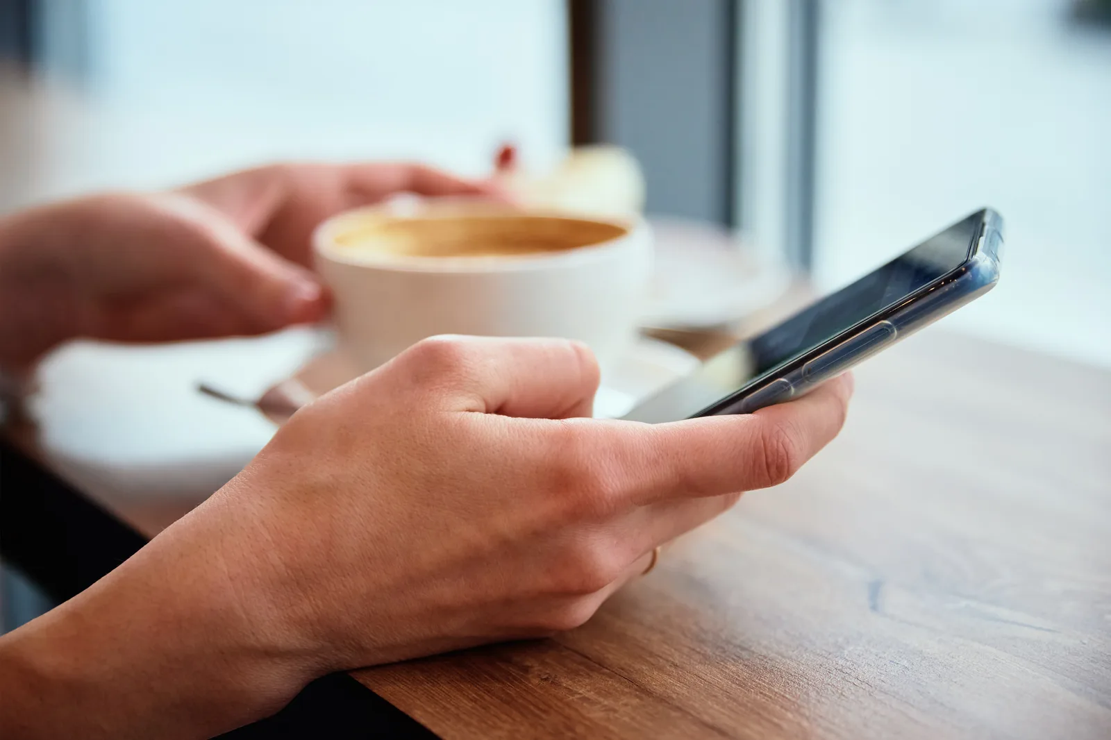 Hands typing a short text on a phone at a cafe table, a coffee beside them