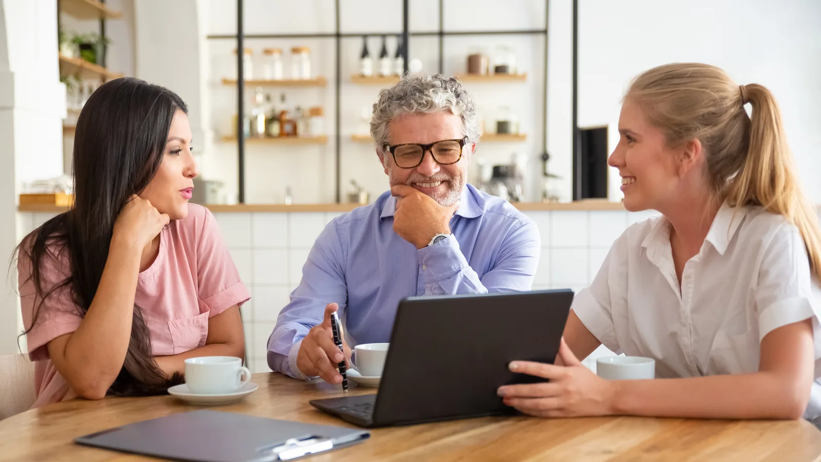 A consultant turns her laptop toward two clients over coffee at a wooden café table
