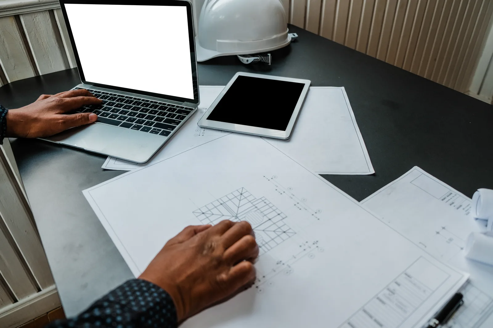 An architect works from a printed plan beside a laptop, the blueprint a snapshot is meant to be