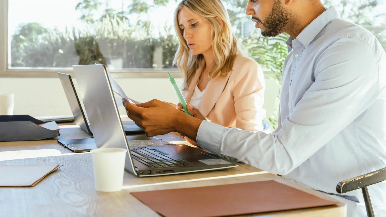 Two colleagues compare printed setup notes against a laptop, checking what a GoHighLevel snapshot carried across