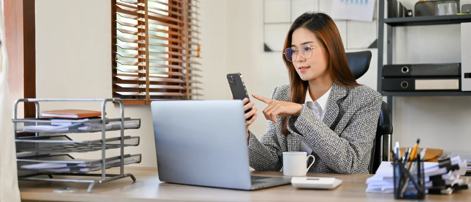 A business owner points at her phone beside an open laptop, reconnecting the accounts a snapshot can't carry