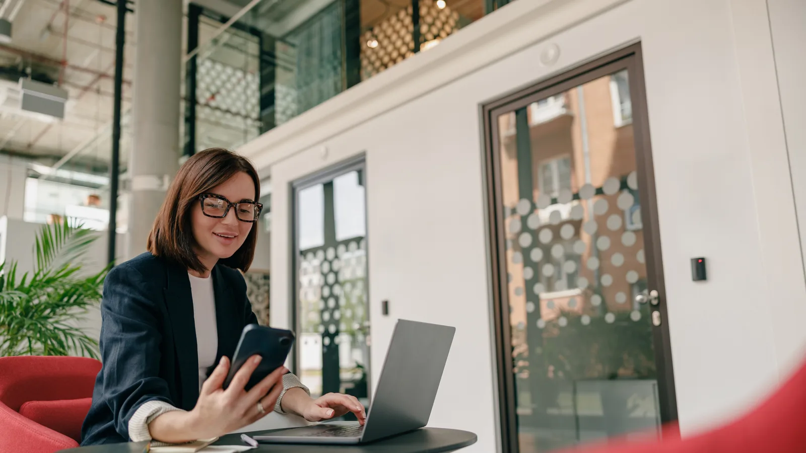 A businesswoman at her desk works across a laptop and a phone at once, the two systems she is trying to connect