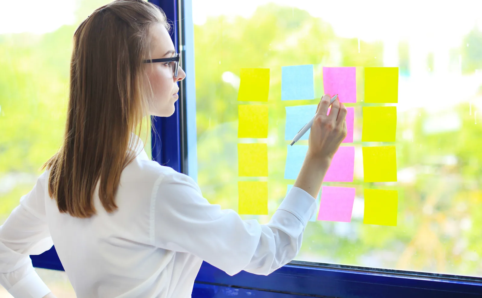 A woman maps a workflow in sticky notes on a glass wall, one note per step