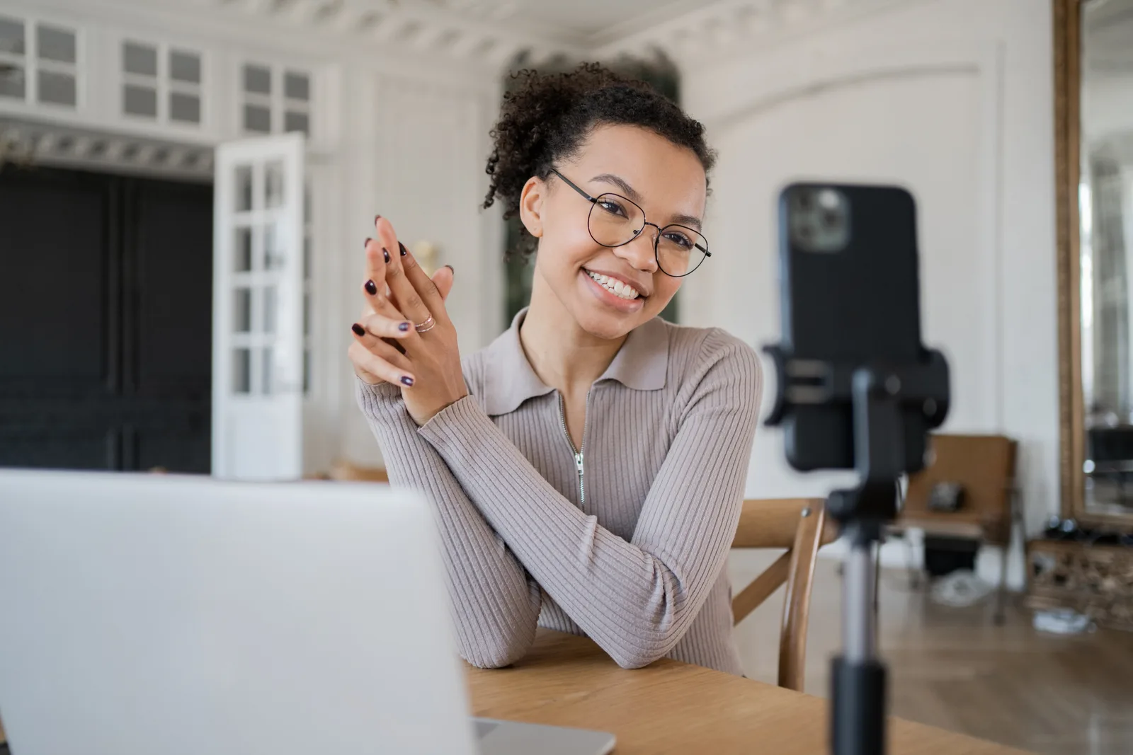 A designer records a short video introduction on a phone set on a tripod, her laptop open on the table