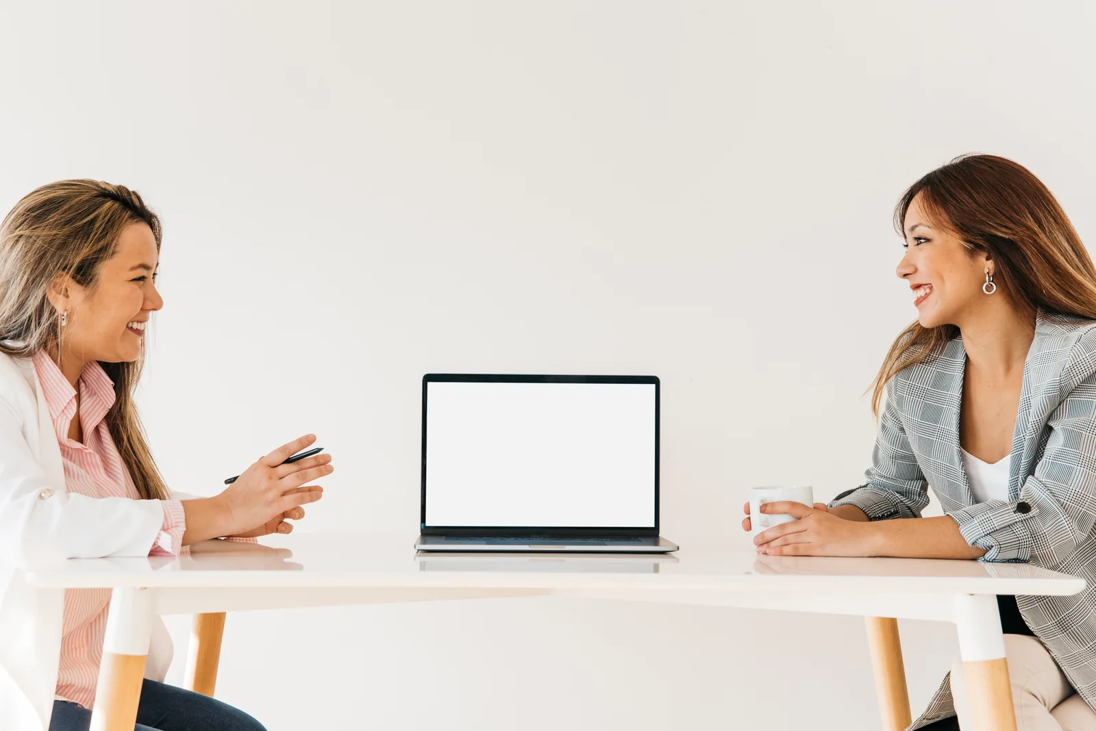 Two women across a table with a laptop between them, talking through the work