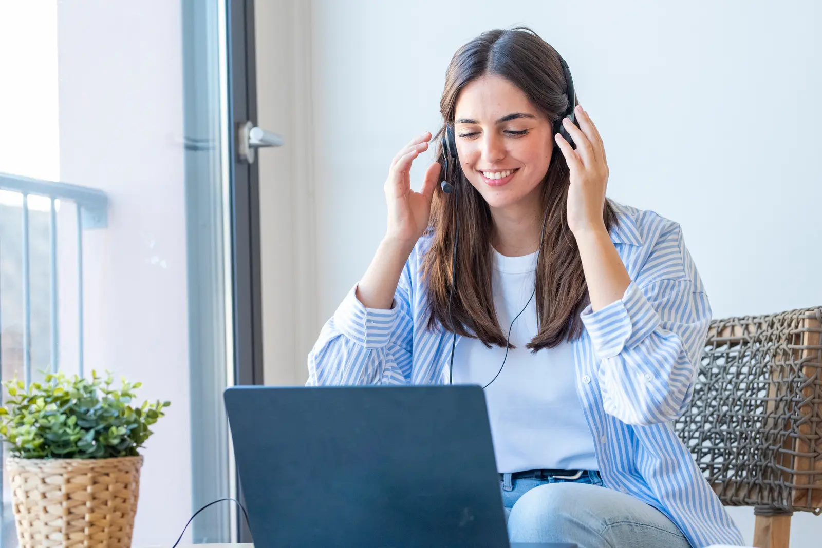 A smiling support agent in a headset takes a call at her laptop by the window