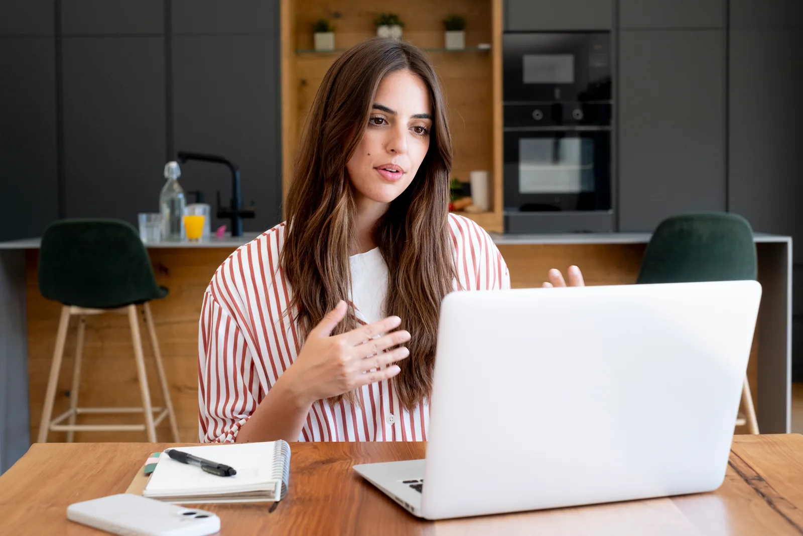 A virtual assistant talks with a client on a video call, notebook and pen beside her laptop at home