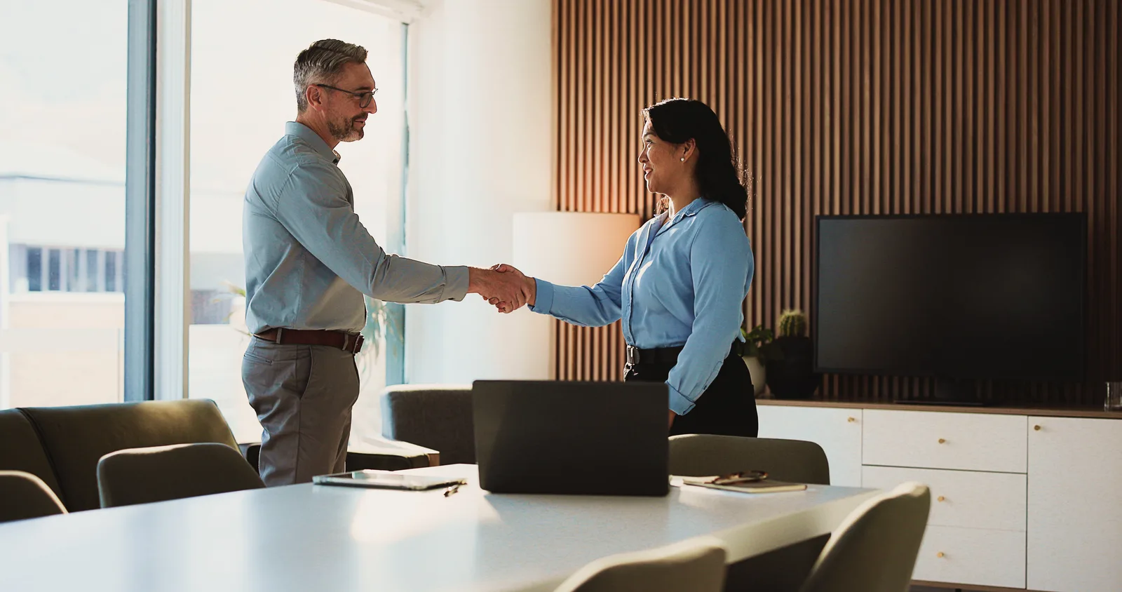 Owner and agency lead shaking hands across a meeting table with a laptop between them
