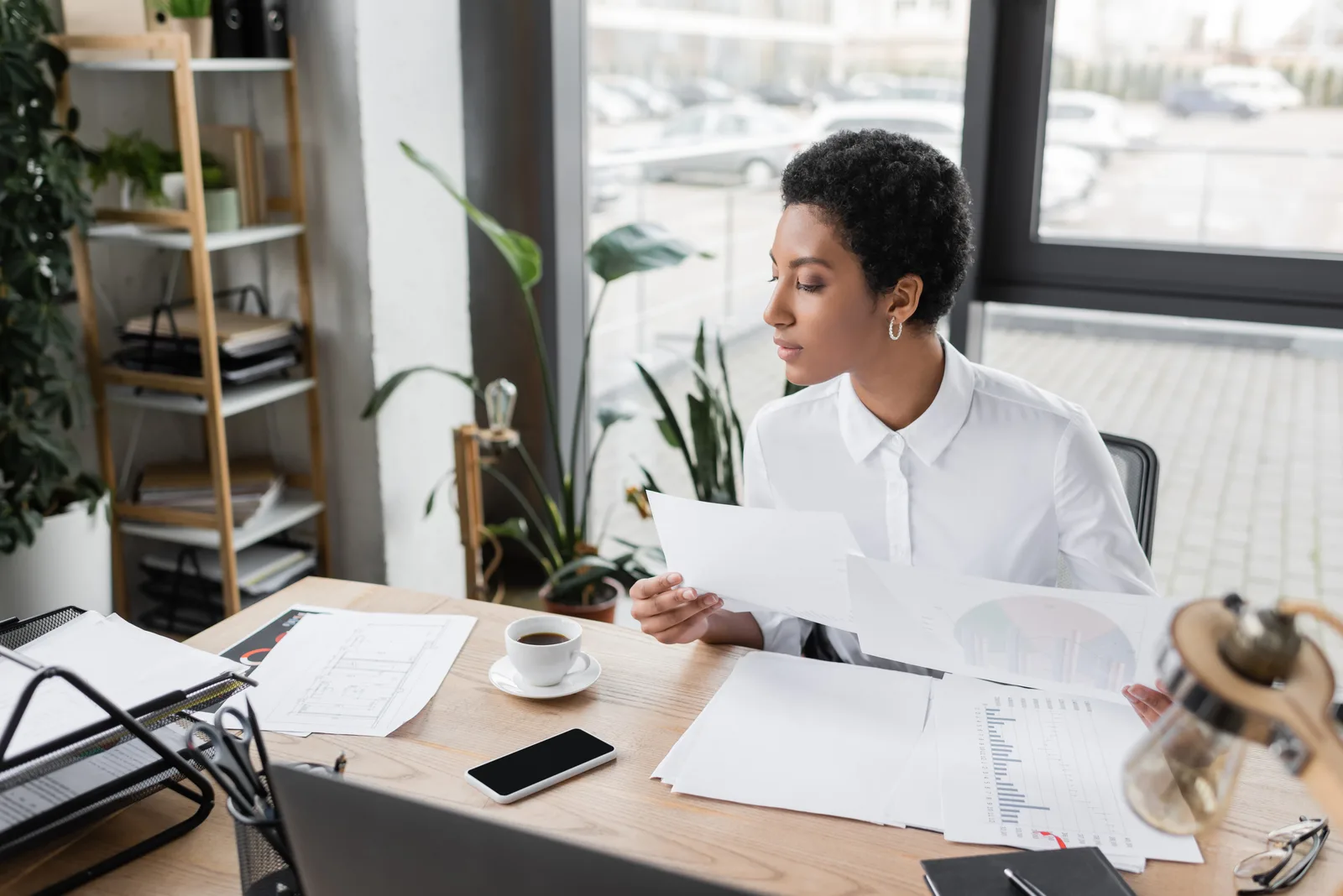 Business owner at her desk comparing two printed proposals beside a coffee and a phone