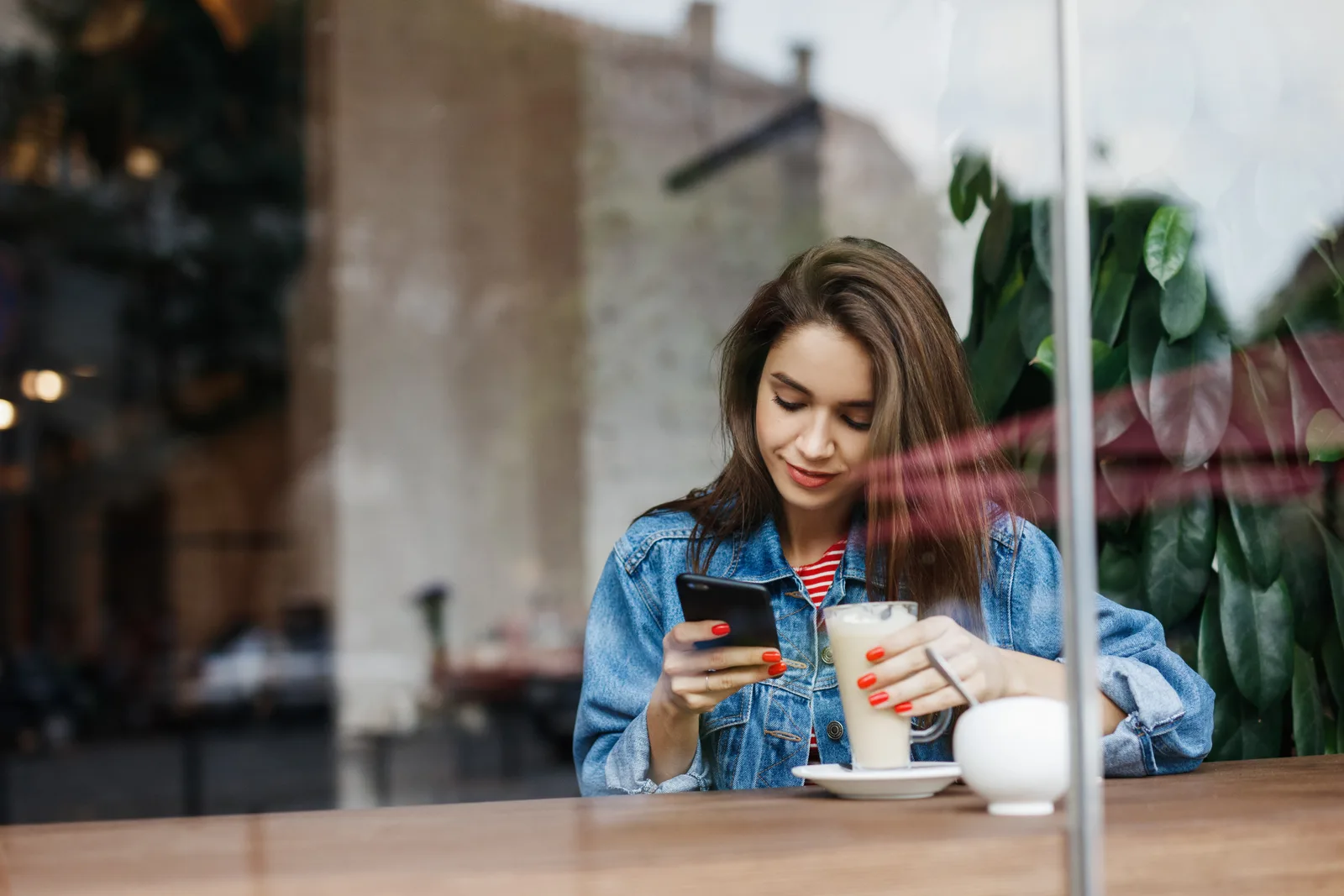 Customer reading reviews on her phone at a cafe window table with a latte beside her