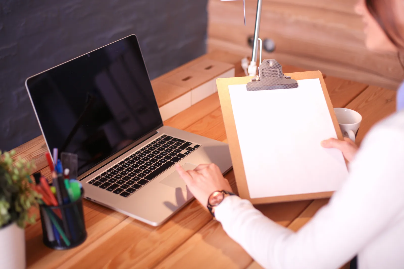 Hand ticking items on a printed checklist on a clipboard next to a laptop