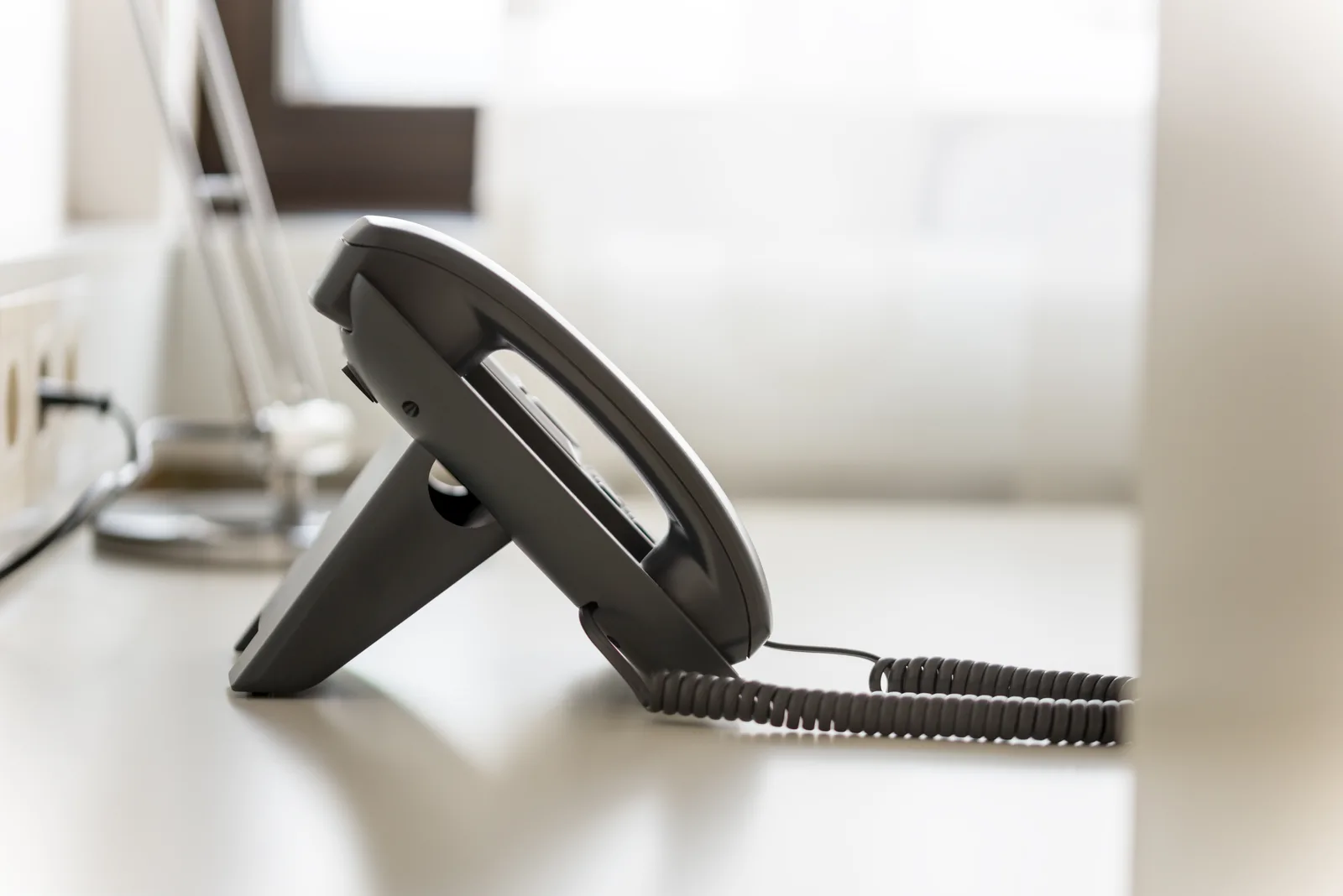 A desk phone on an empty white office desk, nobody there to answer it