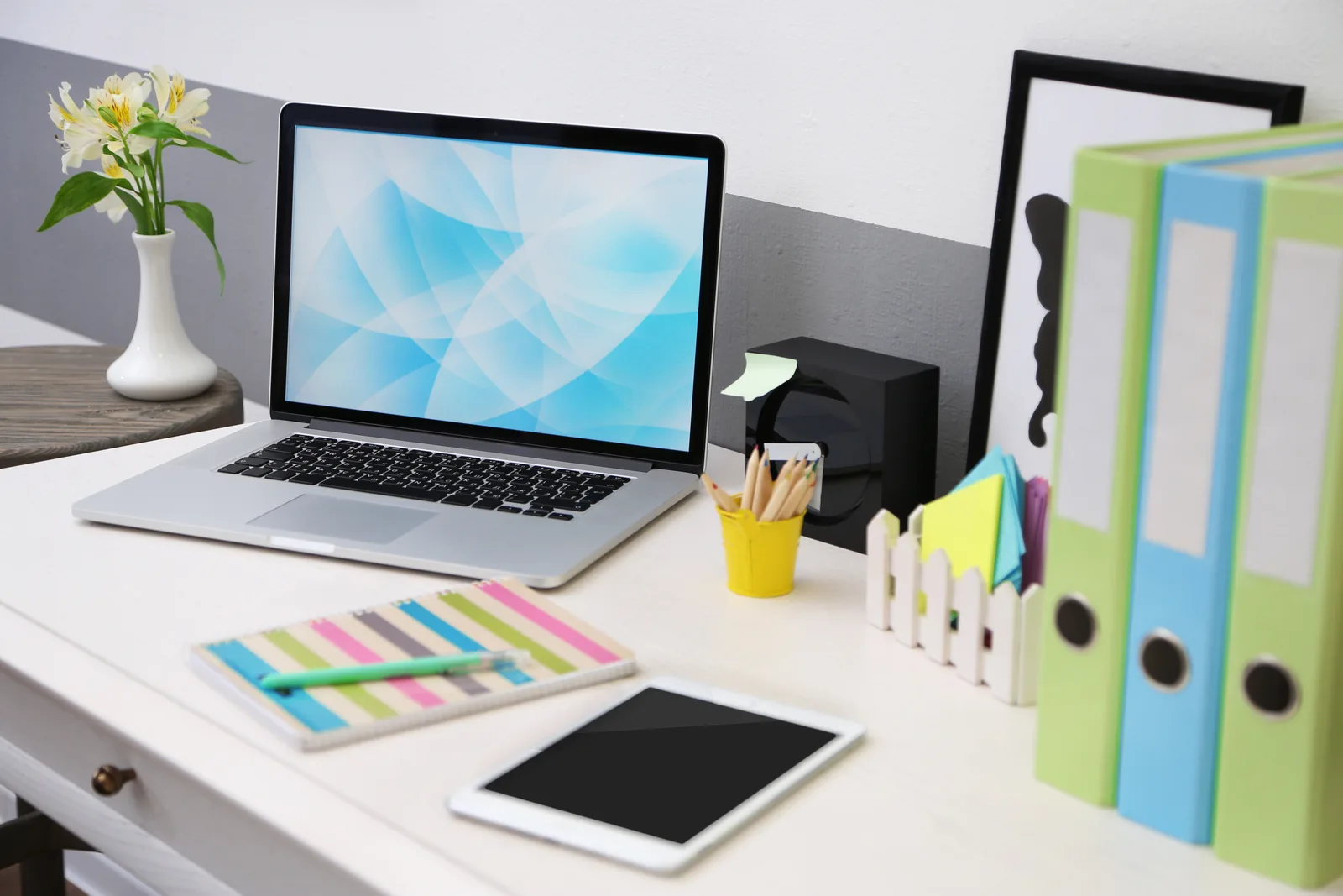 A laptop on a desk beside a row of colour-coded client binders