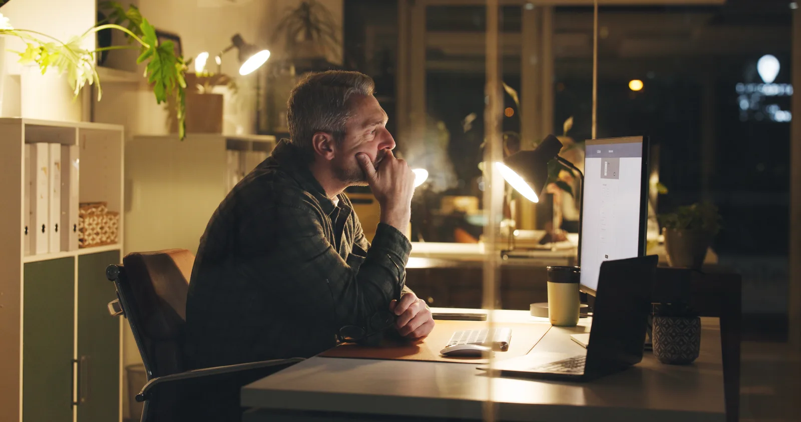 A mature business owner reads on his computer late at night in an empty office