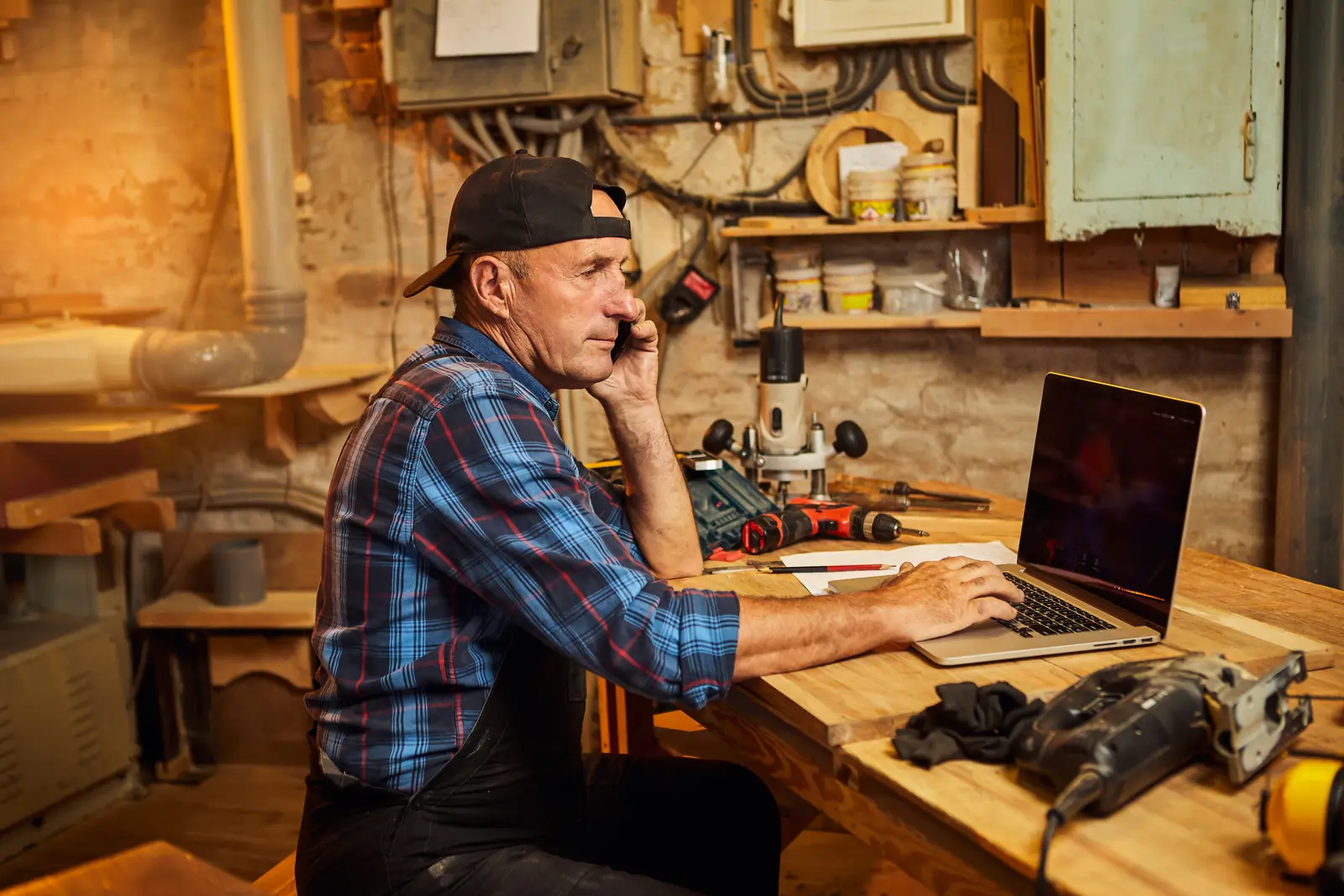 A carpenter at the computer in his workshop, talking a client through the job on the phone