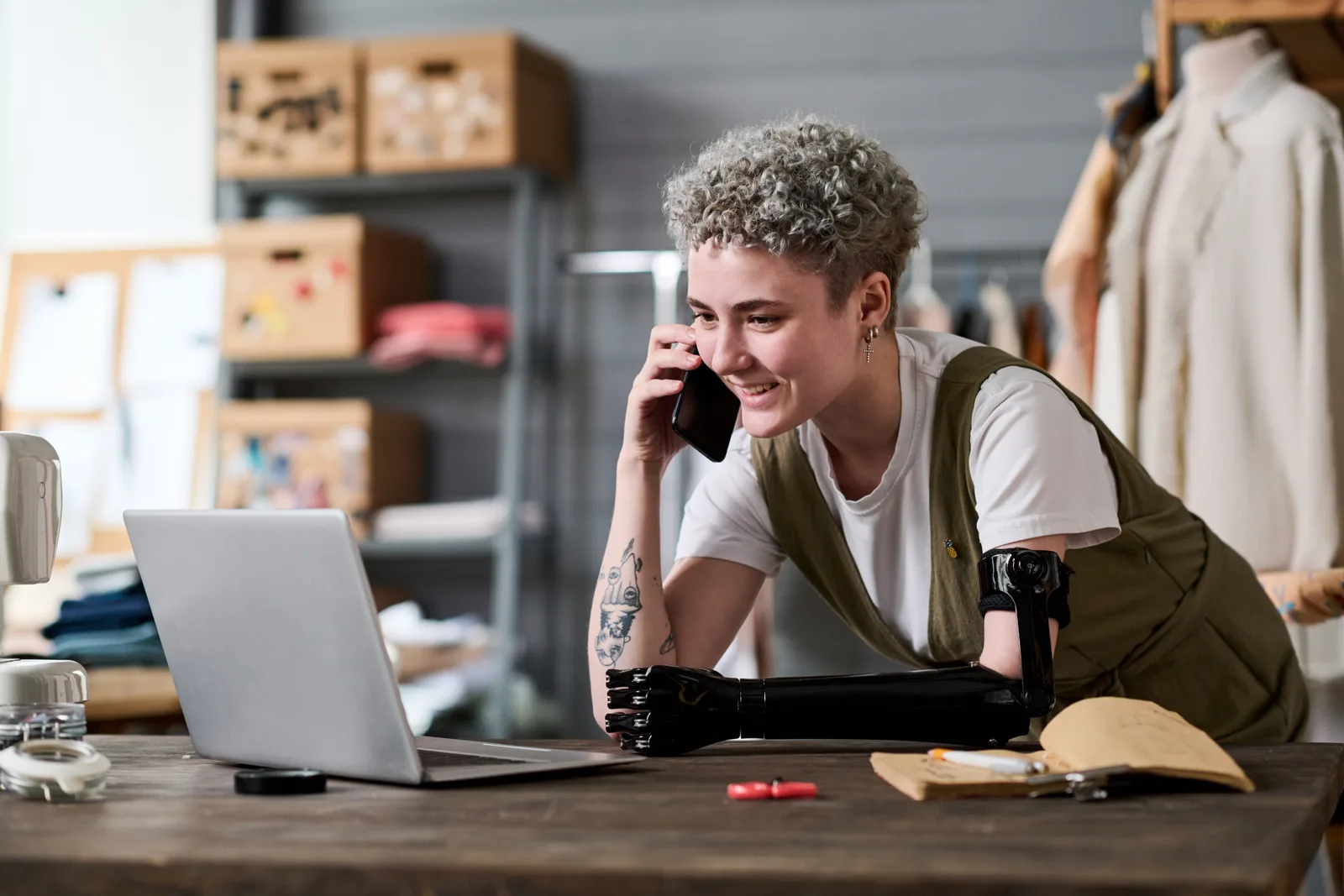 Small business owner takes a phone call at a shop counter beside an open laptop