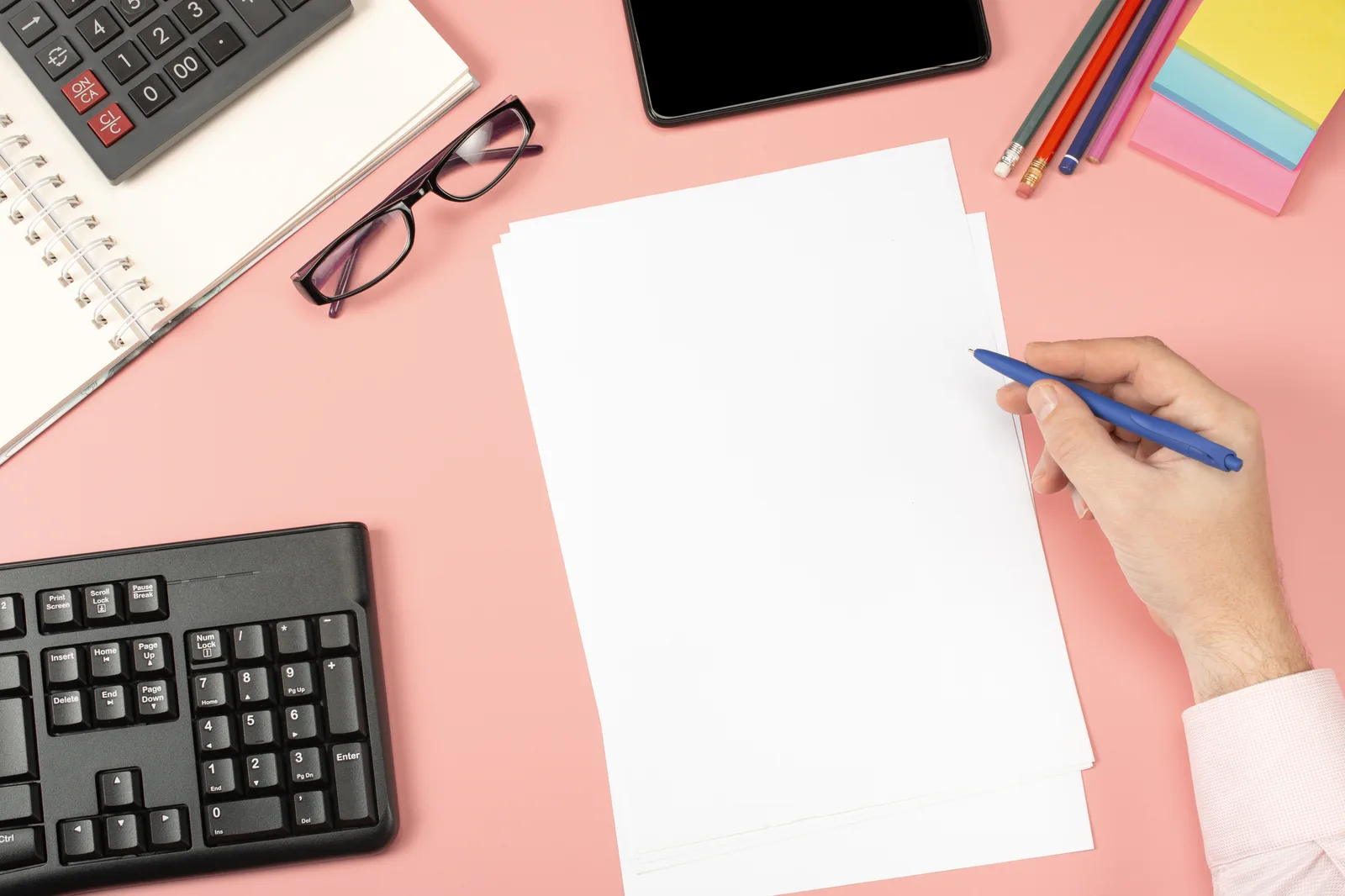 Hands mark up a printed comparison sheet next to a calculator on a wooden desk