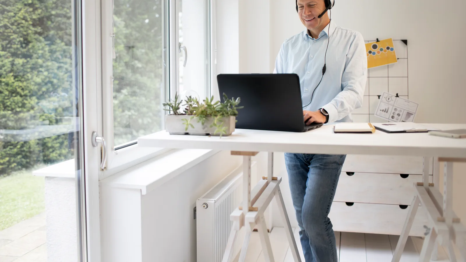 Customer service agent wearing a headset works at a laptop in a small, bright office