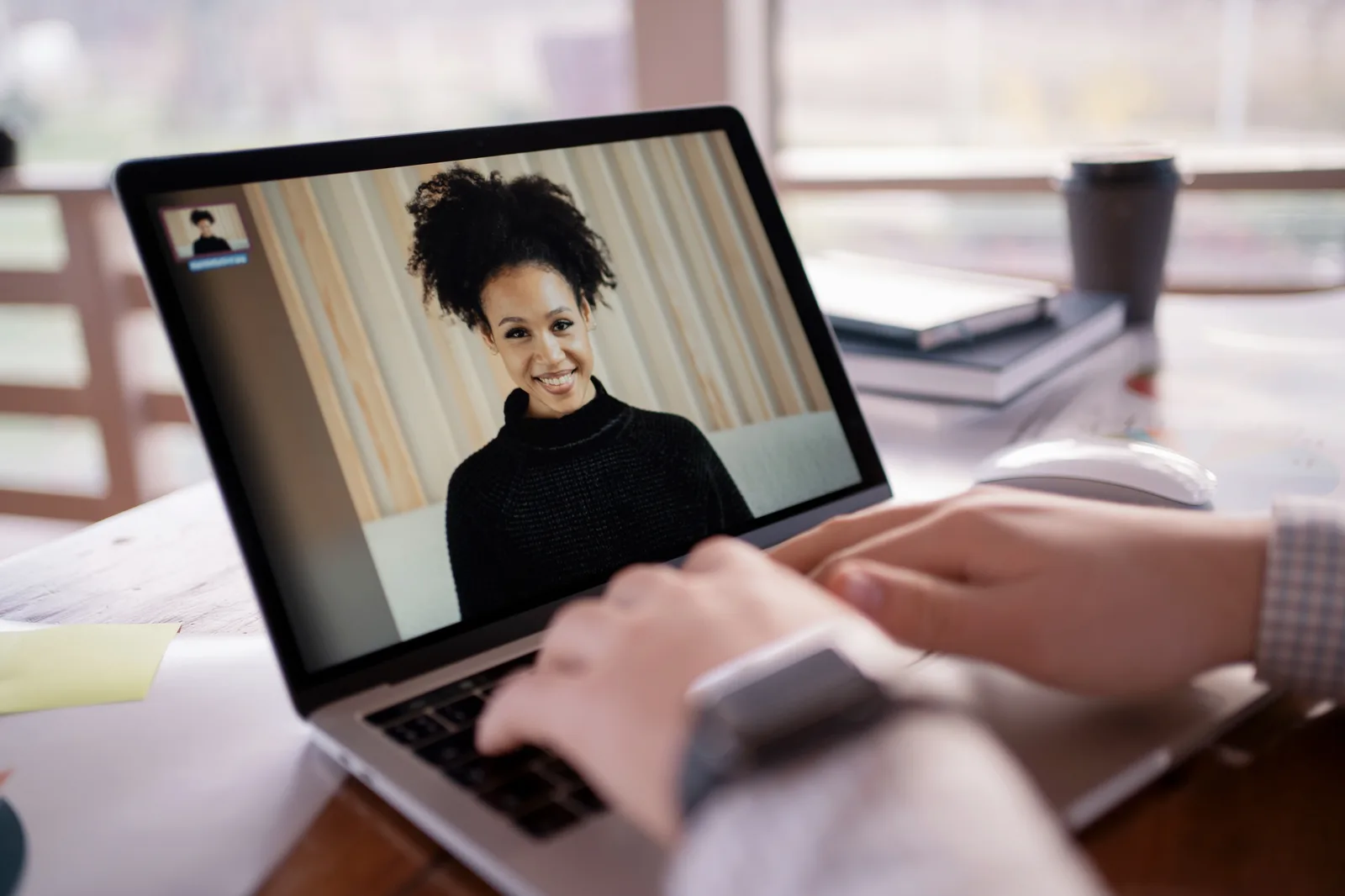Hands rest on a laptop keyboard during a one-to-one video call with a colleague on screen