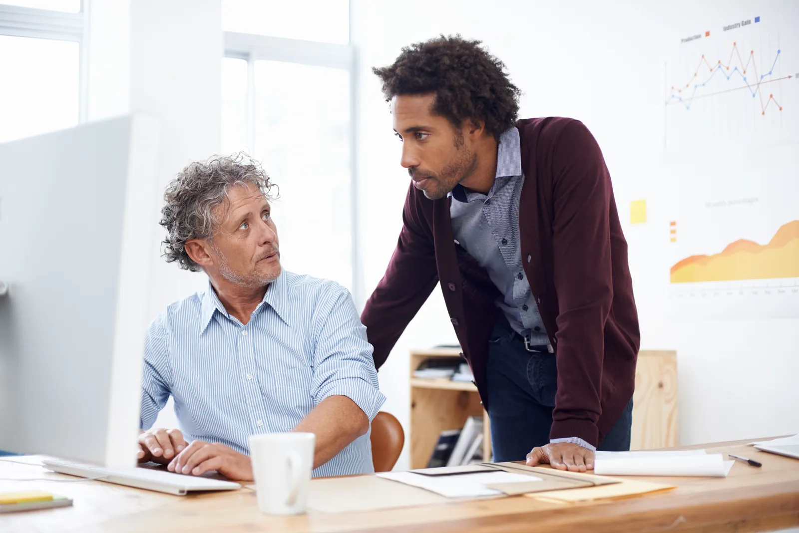 A colleague leans in to point at a desktop screen while a business owner works at the keyboard